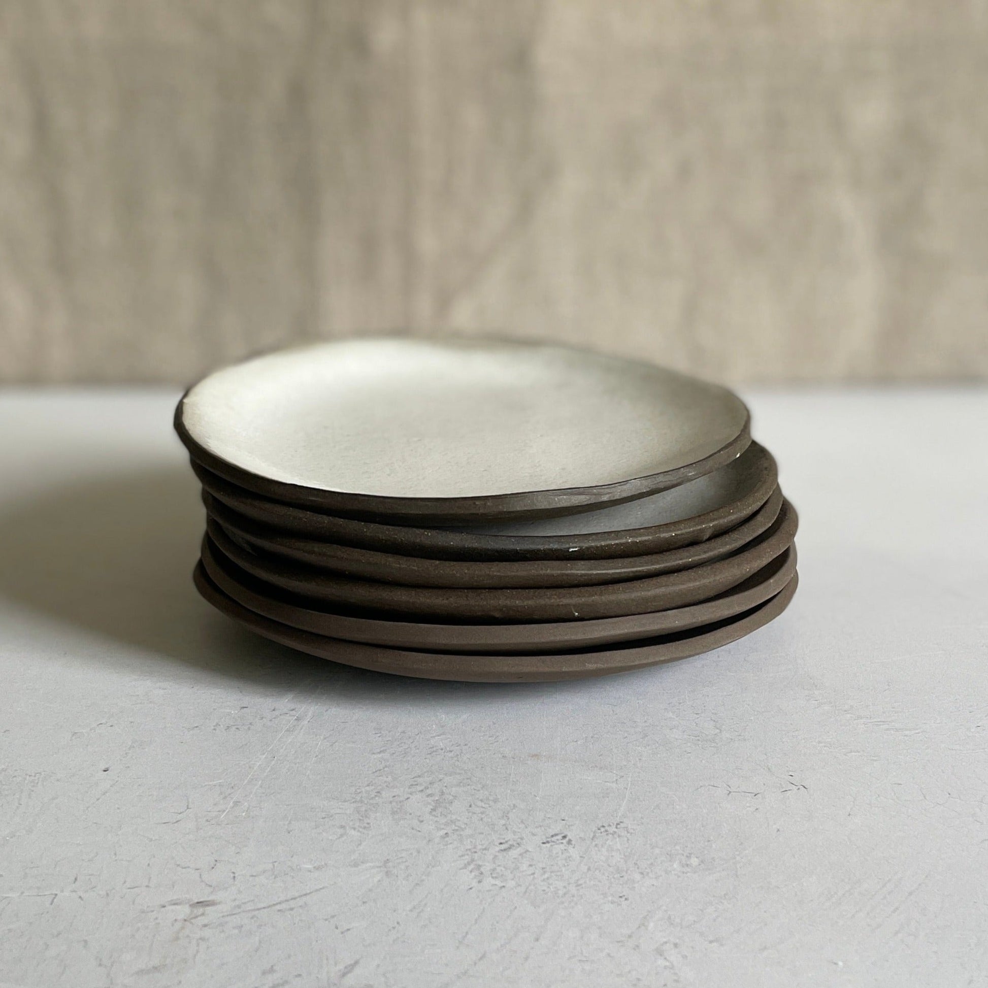 stack of six white handmade ceramic salad plates dark edges